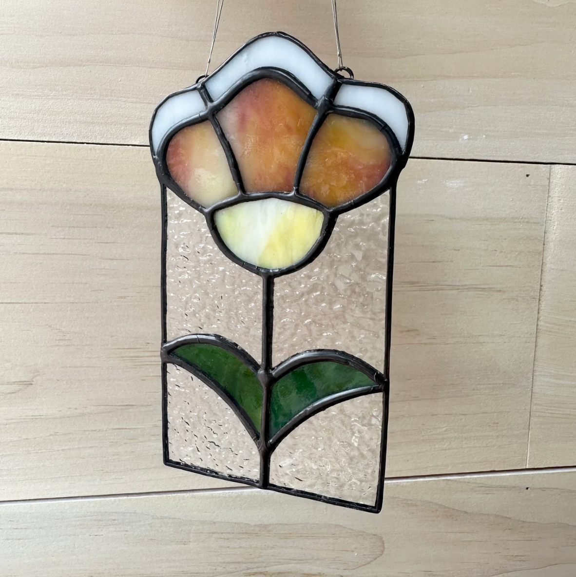 A stained glass sun-catcher of an orange flower.