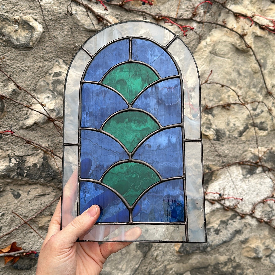 Geometric stained glass art piece up against a stone wall.