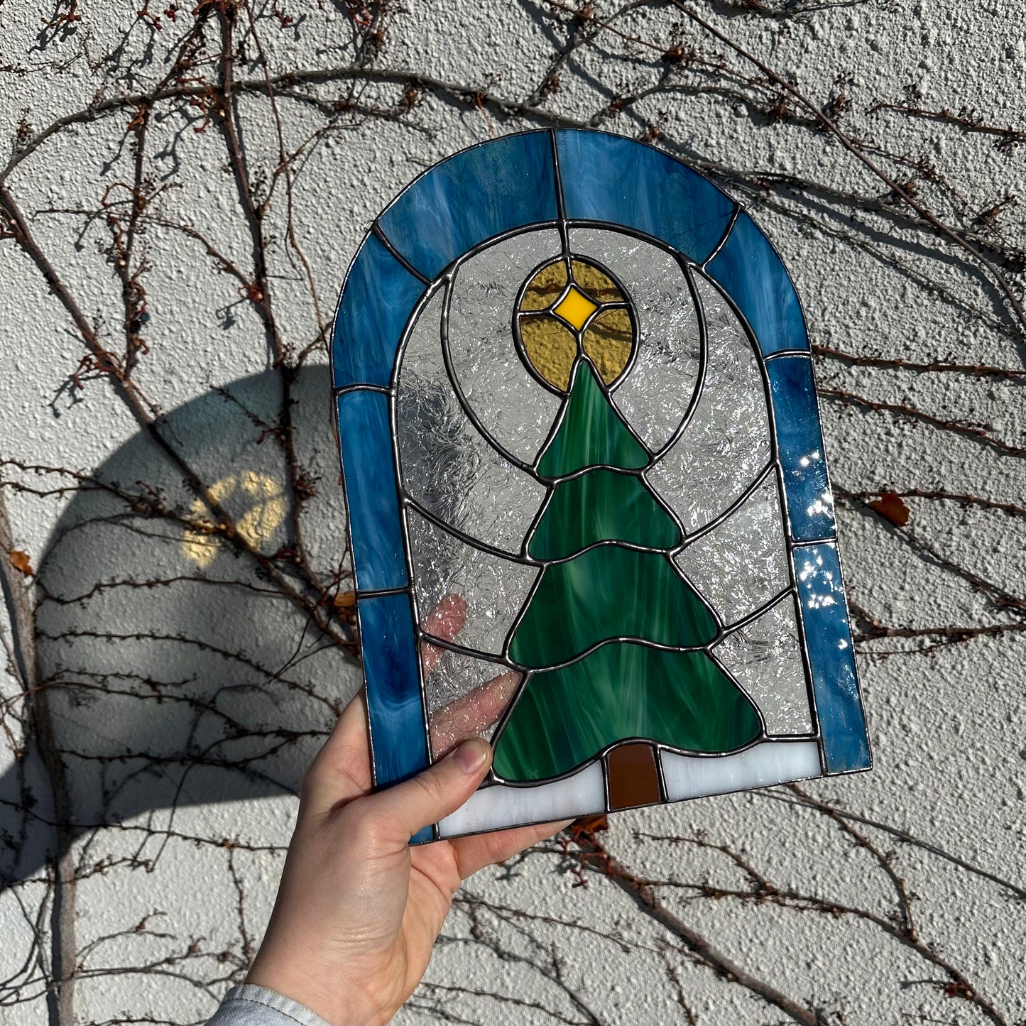 A stained glass window of a pine tree in a snowy field.