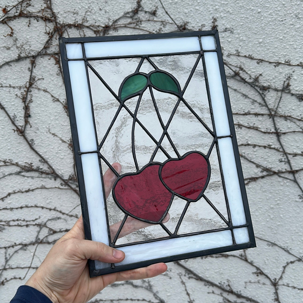 A stained glass window of two red heart-shaped cherries with a white border.
