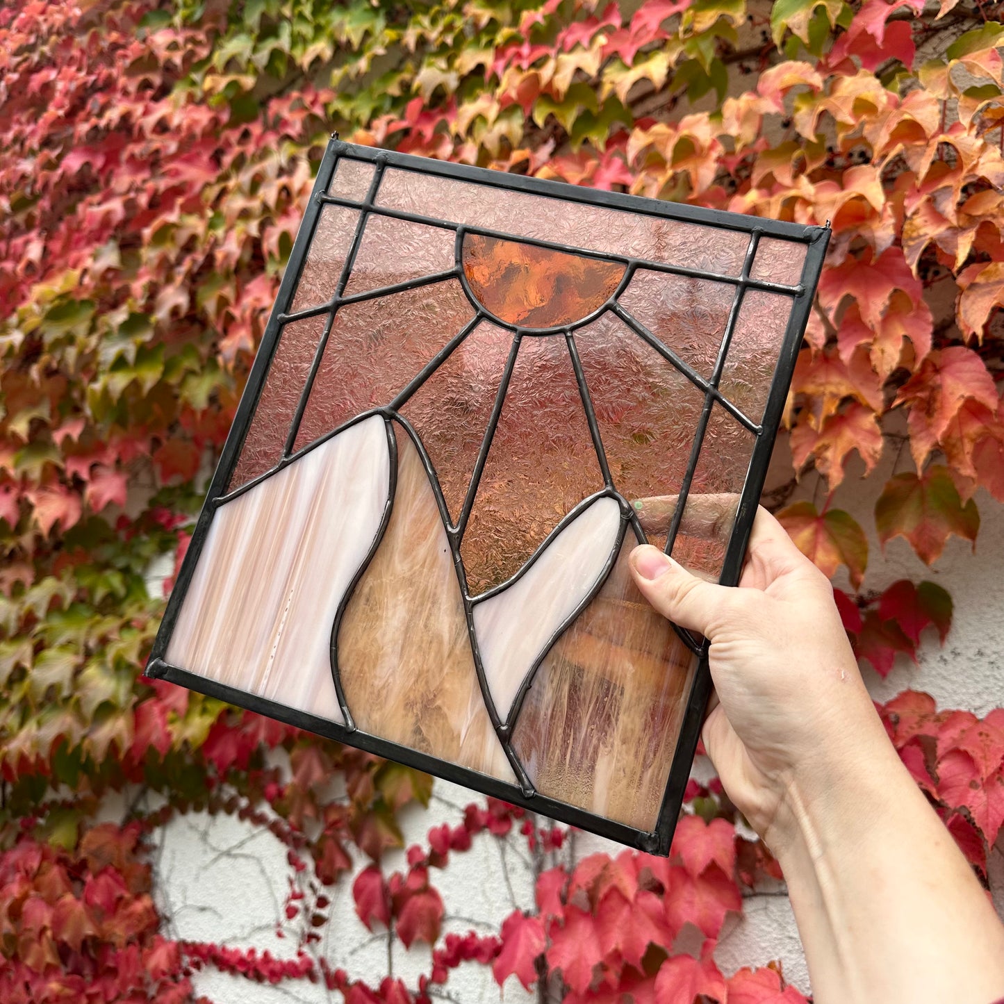 A stained glass window of mountains and sun rays.