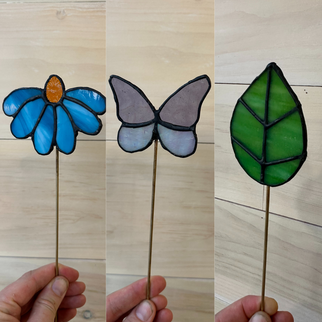 A set of three stained glass plant stakes, a flower, a butterfly and a leaf.