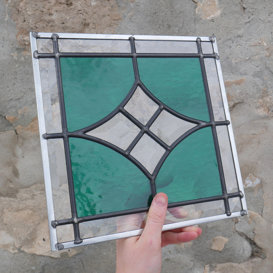 Stained glass panel with geometric design held against a stone wall.