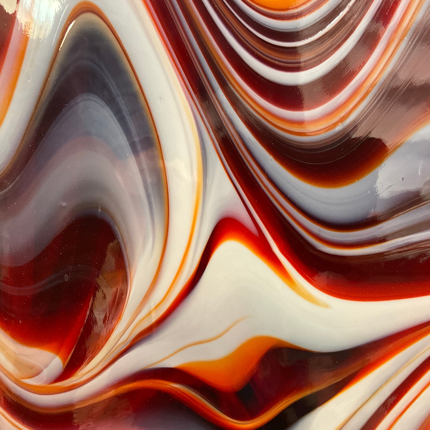 A close-up image of fused glass with swirls of red, orange, white, and brown, showcasing a smooth texture and opal art effect.