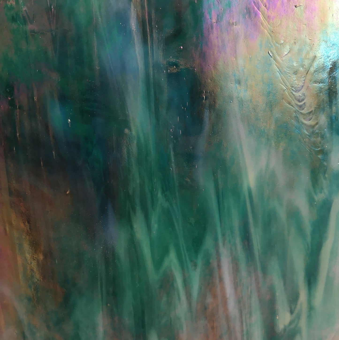 A close-up image of a teal colored non-fusible art glass with an iridescent finish displaying a range of colors including purple and green.