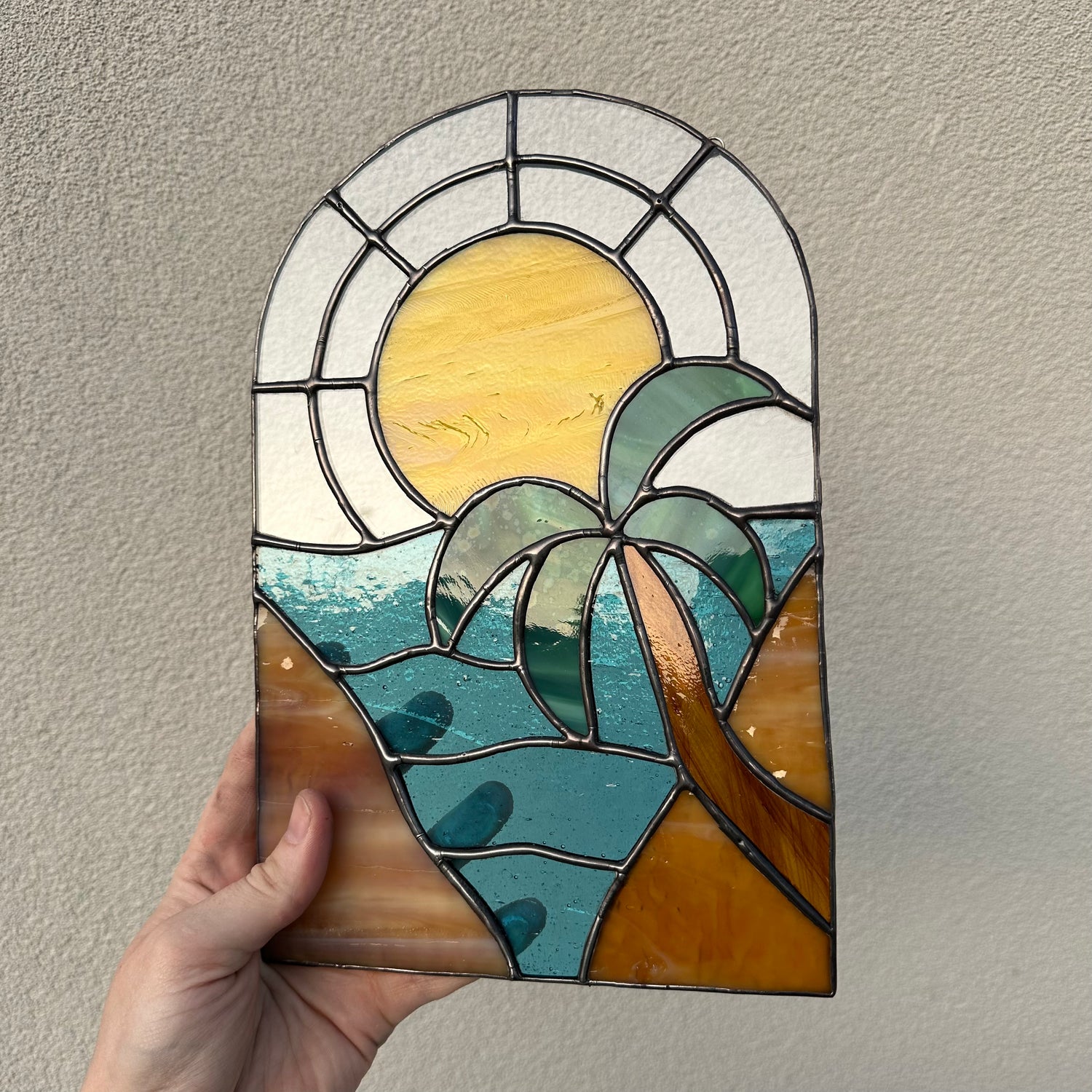 A stained glass pattern of a sunset with a palm tree.