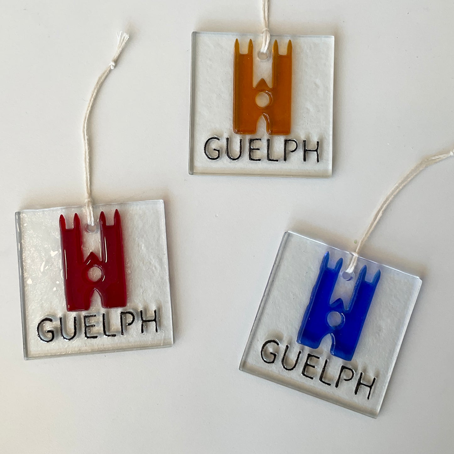 Fused glass ornaments with the word Guelph at the bottom of a square of clear glass with colourful outlines of the basilica above