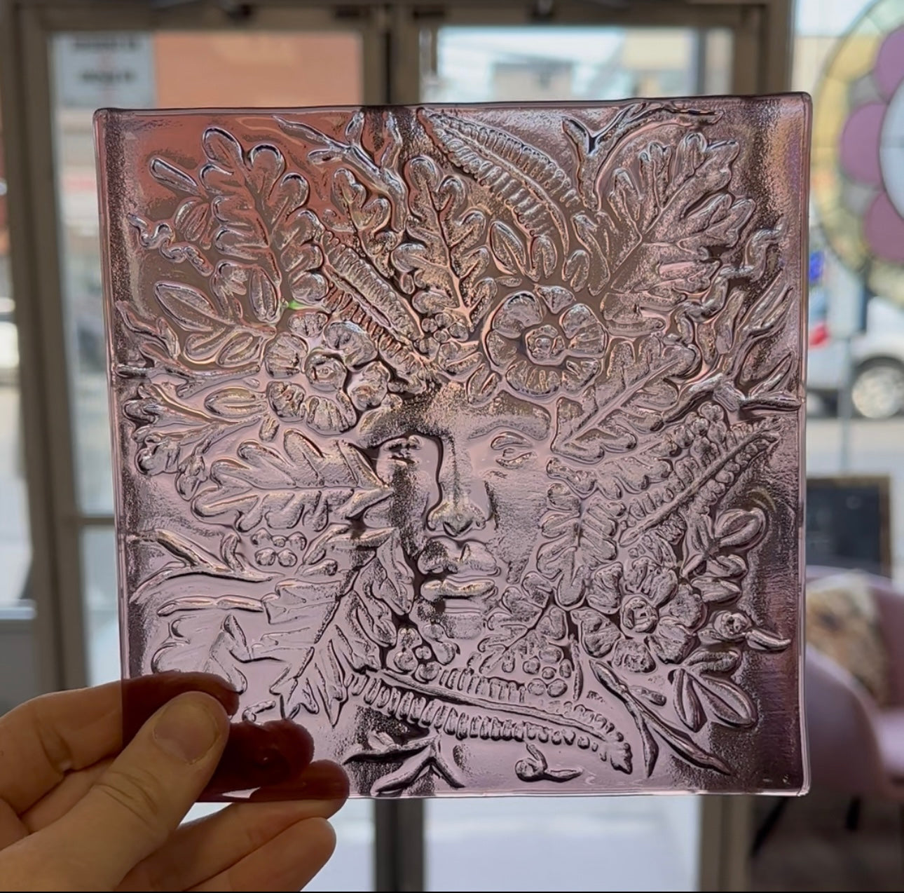 A piece of purple textured glass with a ladies face surrounded by foliage.