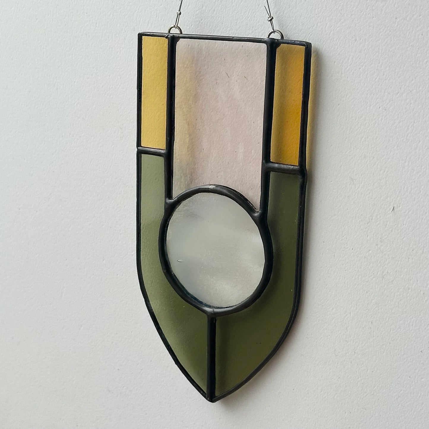 Geometric stained glass sun catcher against a white wall.