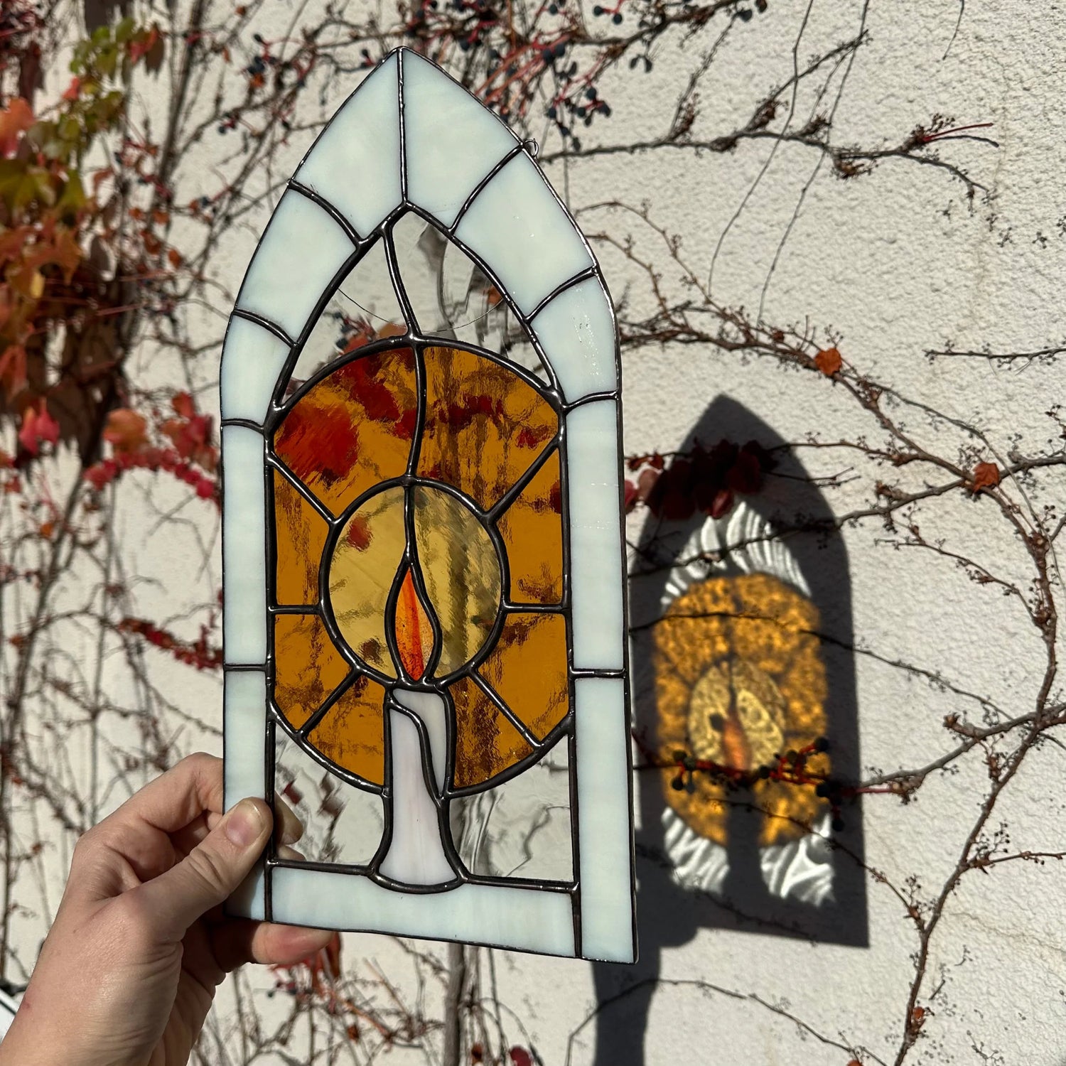 A stained glass window of a candle glowing in an arch frame.