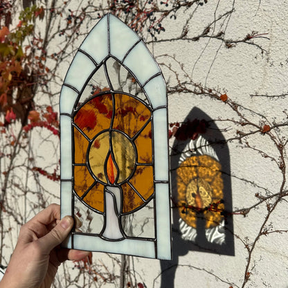 A stained glass window of a candle glowing in an arch frame.