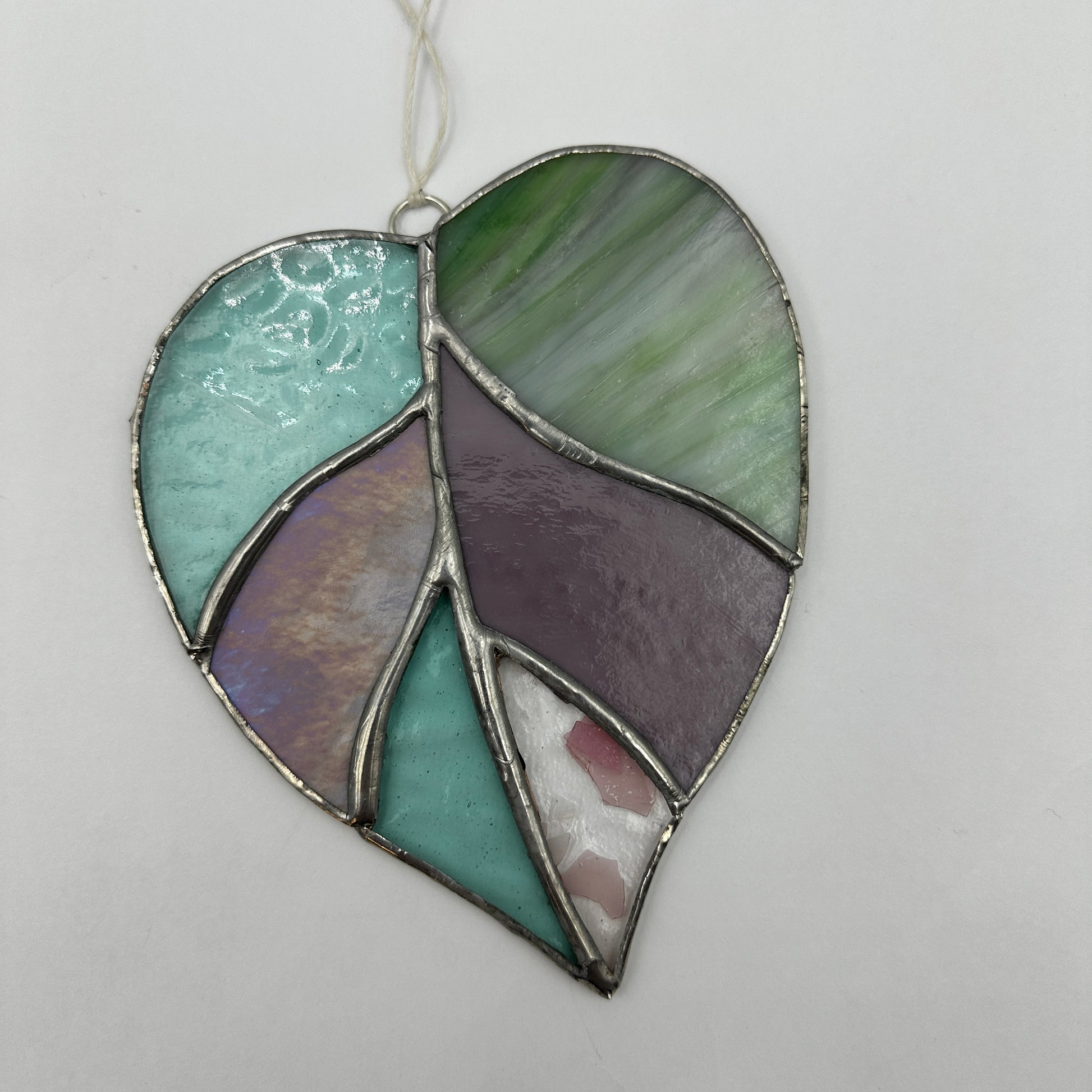 Stained glass leaf-shaped ornament with green and purple hues on a light gray background