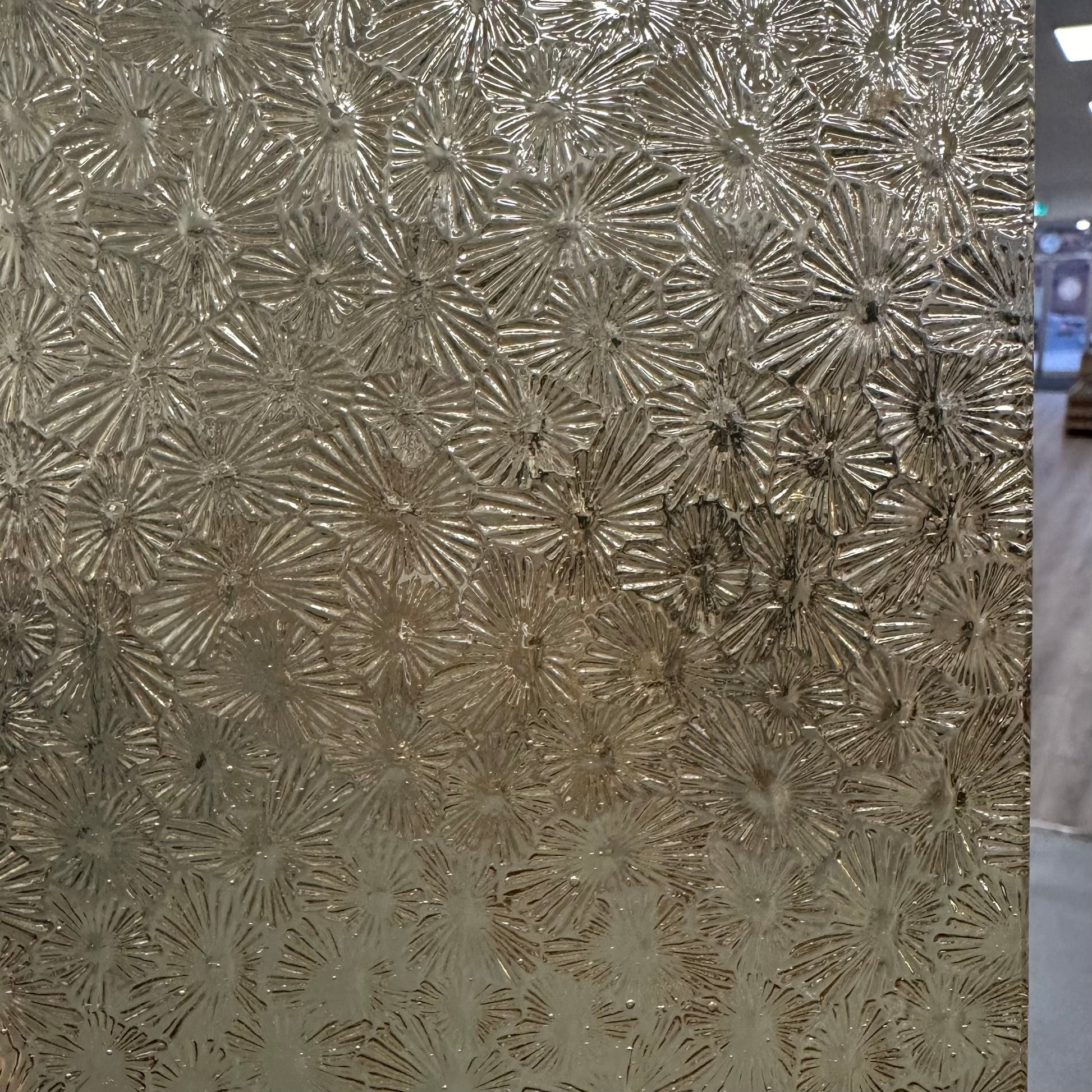 A close-up image of a textured, pale amber colored art glass panel with a floral pattern.
