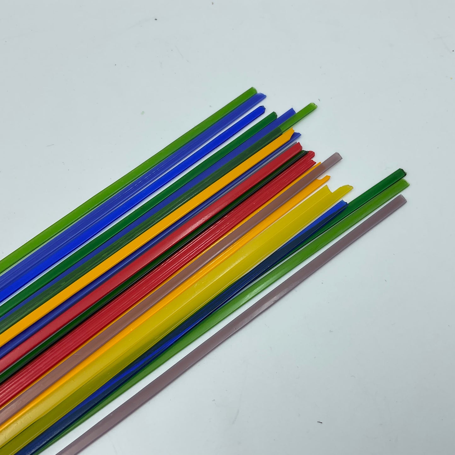 A collection of colorful glass noodles laid out on a white surface, featuring a variety of colors including yellow, red, blue, green, and purple.