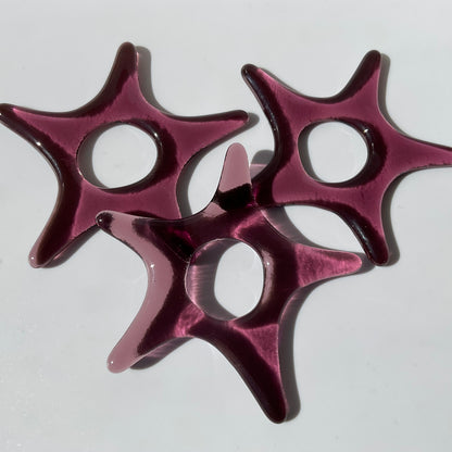 Three purple fused glass star ornaments.