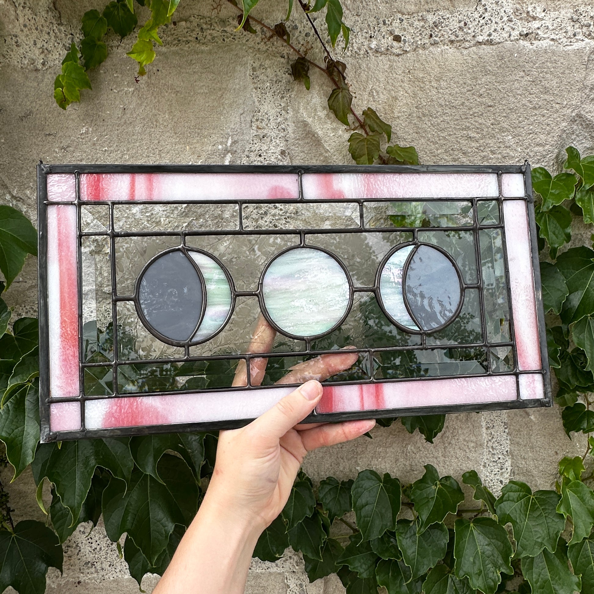 Stained glass panel held by a hand with ivy in the background