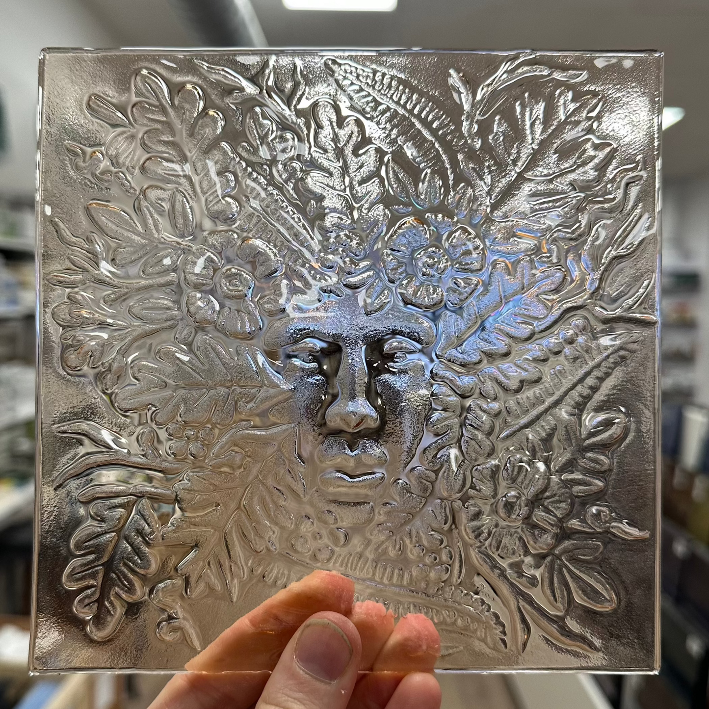 A piece of textured fused glass with a woman's face surrounded by foliage.
