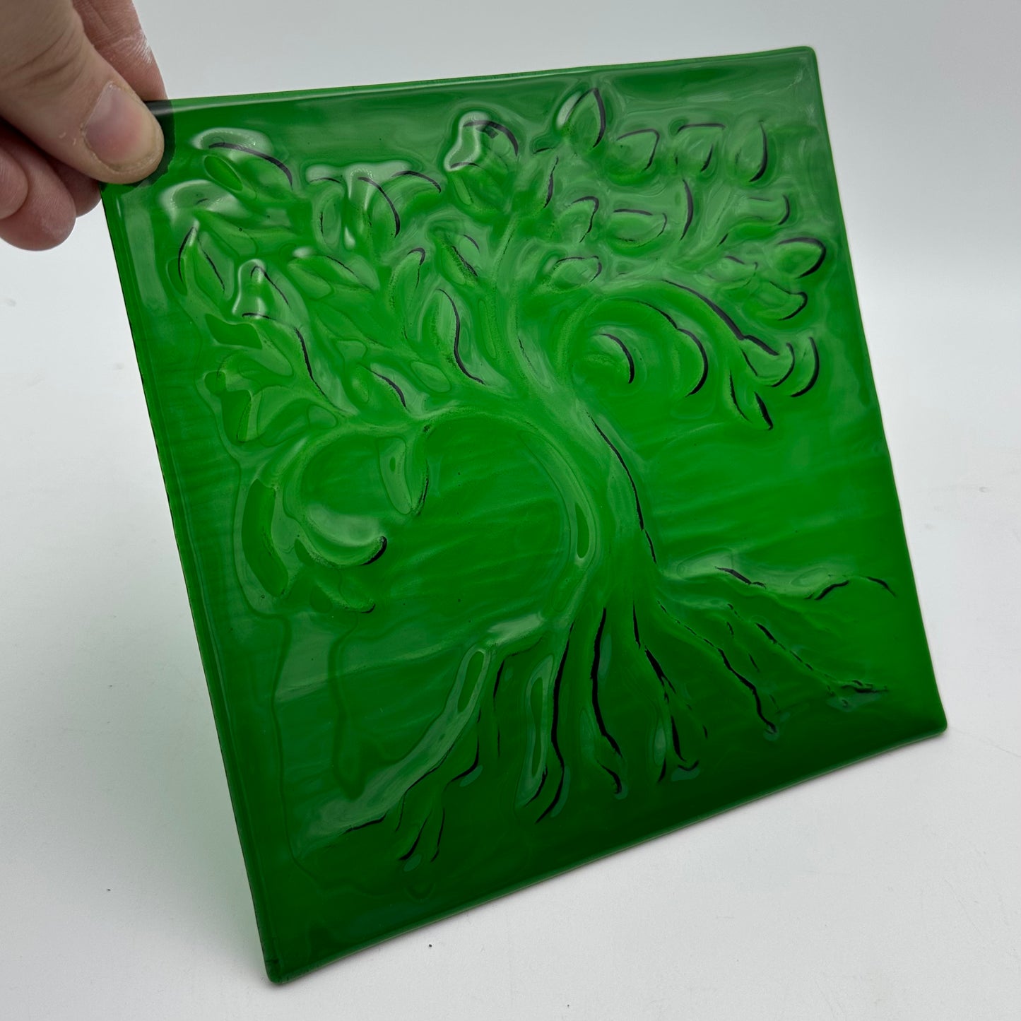 A textured piece of green fused glass with a tree.