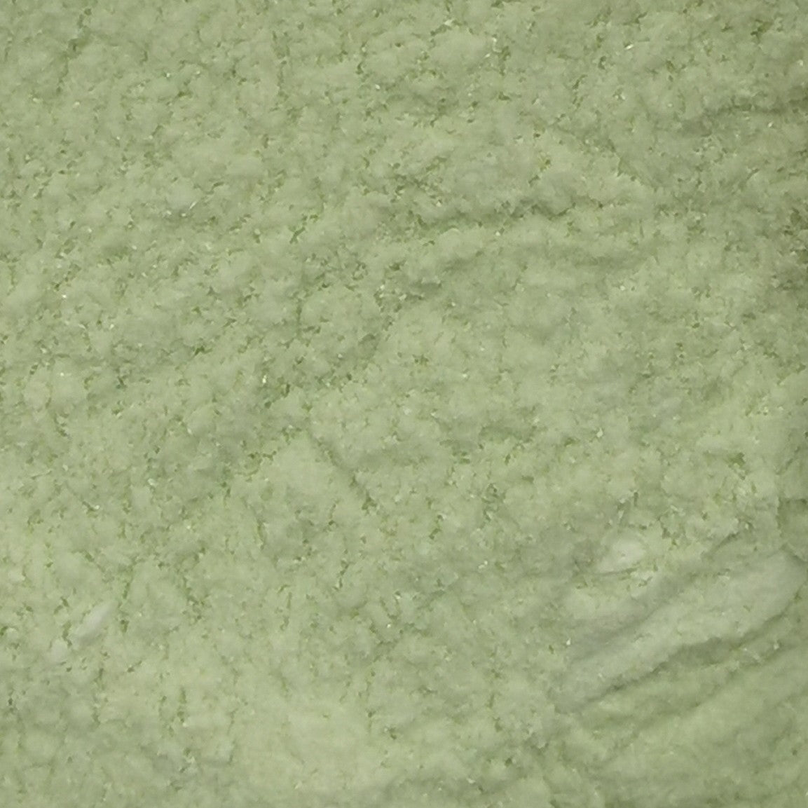 Close-up of an 8oz bottle of OGT Amazon Green Opal 2264 System 96 frit, showing the texture and green color of the material.