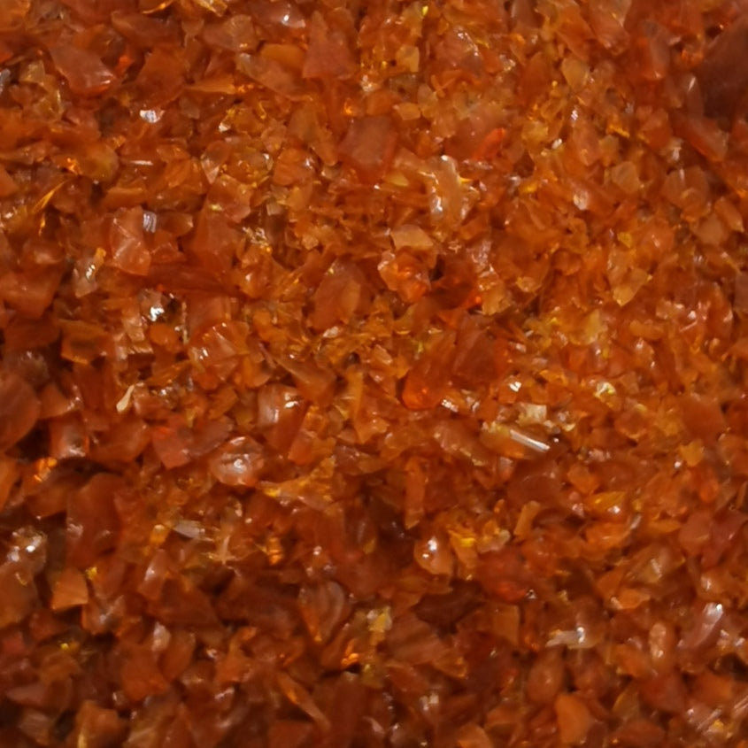 A close-up of a bottle filled with yellow-colored frit, which is a type of opal used in glassmaking.