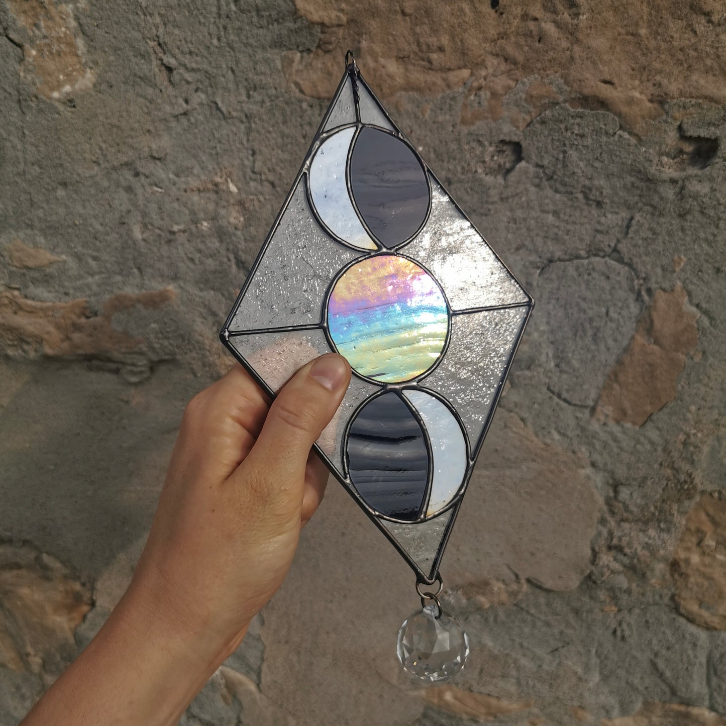 Stained glass suntcaher with a moon design held up against a limestone wall.